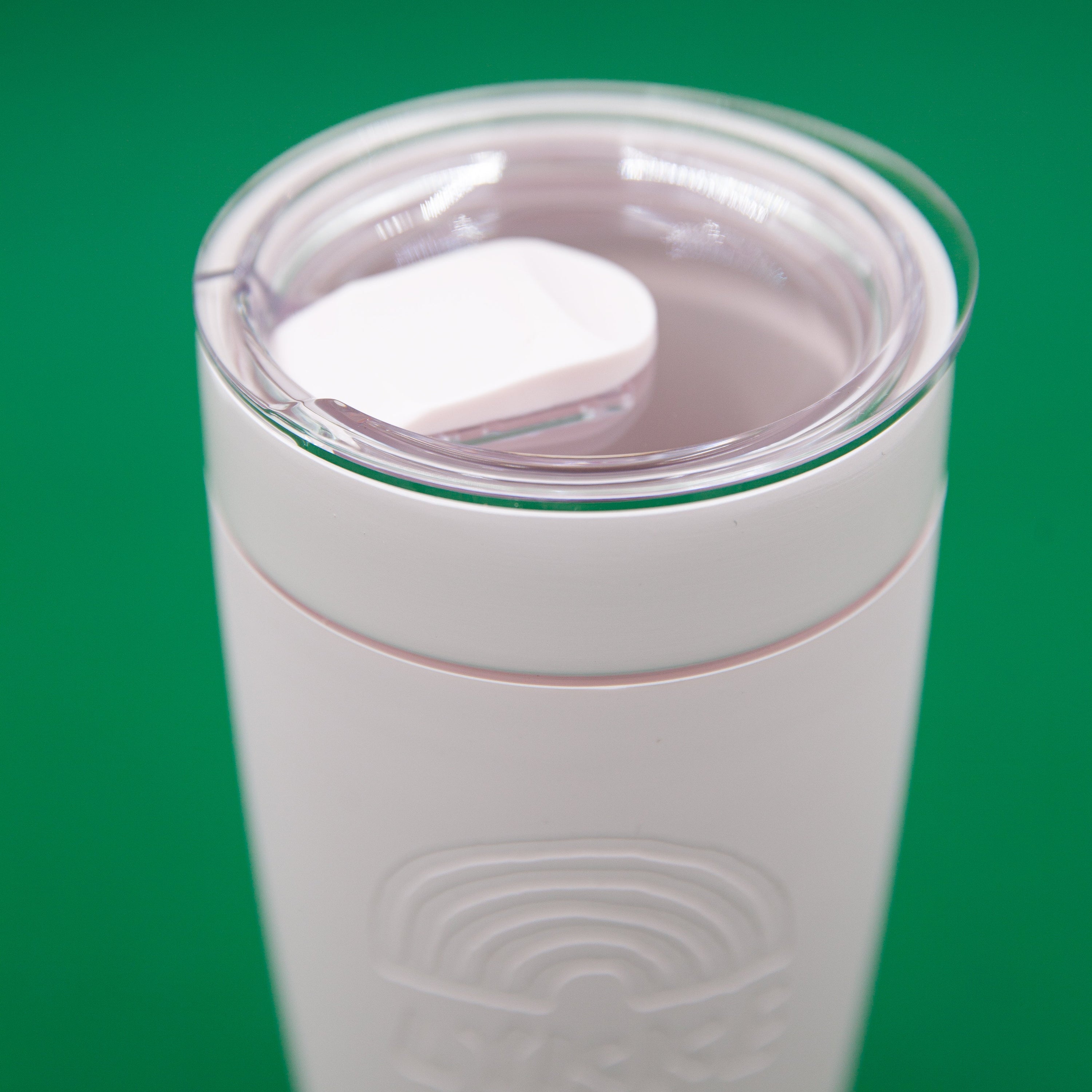 Pink tumbler with a clear lid on a green background