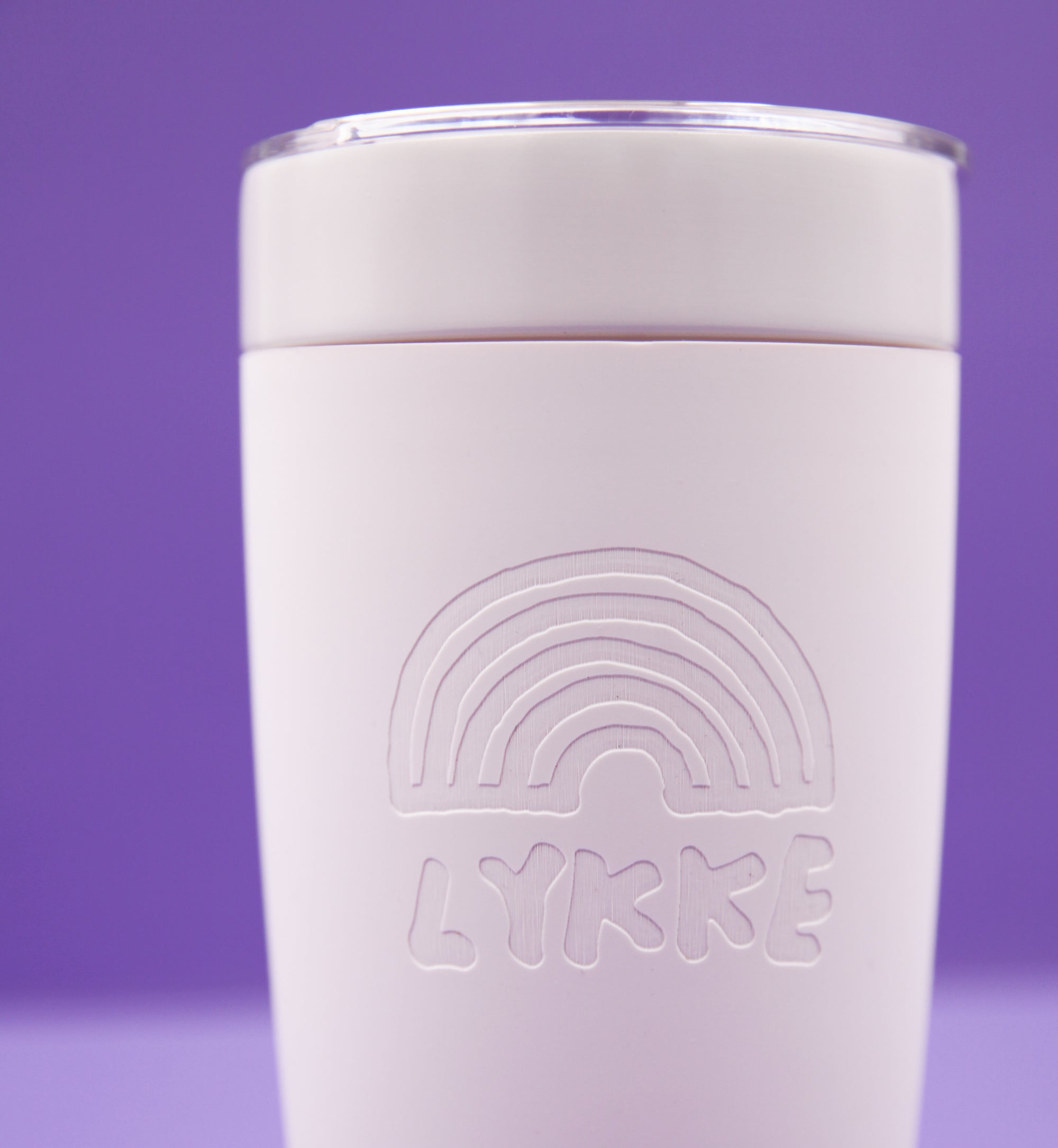 Pink tumbler with embossed rainbow design and 'LYKKE' branding on a purple background